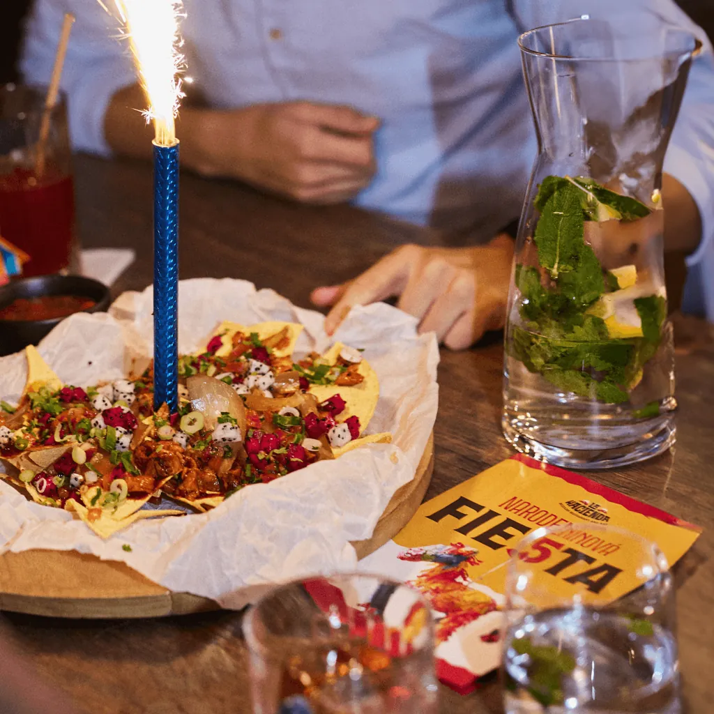 Nachos with a sparkler candle at La Hacienda, beside a birthday fiesta card and a mint water carafe
