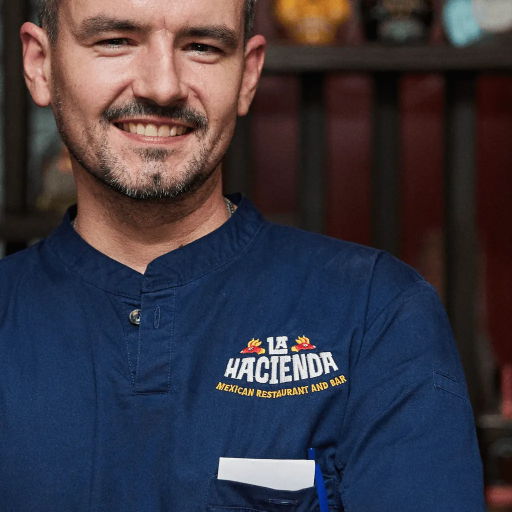 A smiling La Hacienda staff member in a navy shirt with the embroidered logo