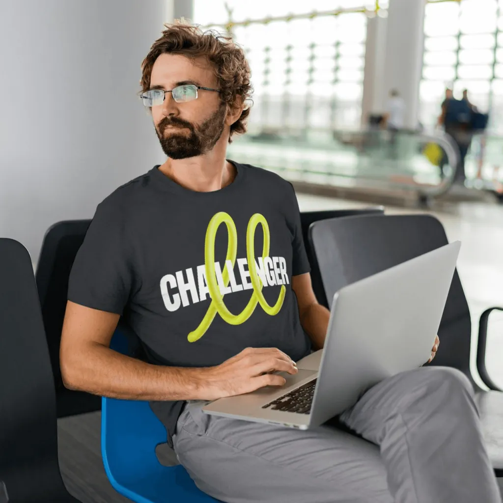 A man working on a laptop in a Challenger T-shirt with the yellow loop